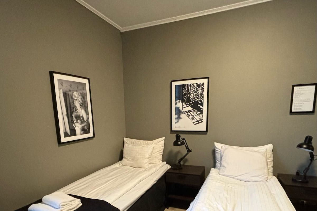 A twin room with two single beds, a nightstand, a desk, and two framed pictures on the wall.