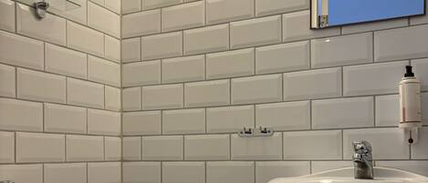 Un baño con azulejos blancos tipo metro, un inodoro, un lavamanos, un espejo y un dispensador de papel higiénico.