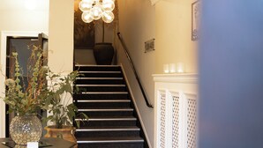 A staircase with a checkered floor, a vase with plants on a table, and a chandelier. - Hotell Esplanad (Växjö)