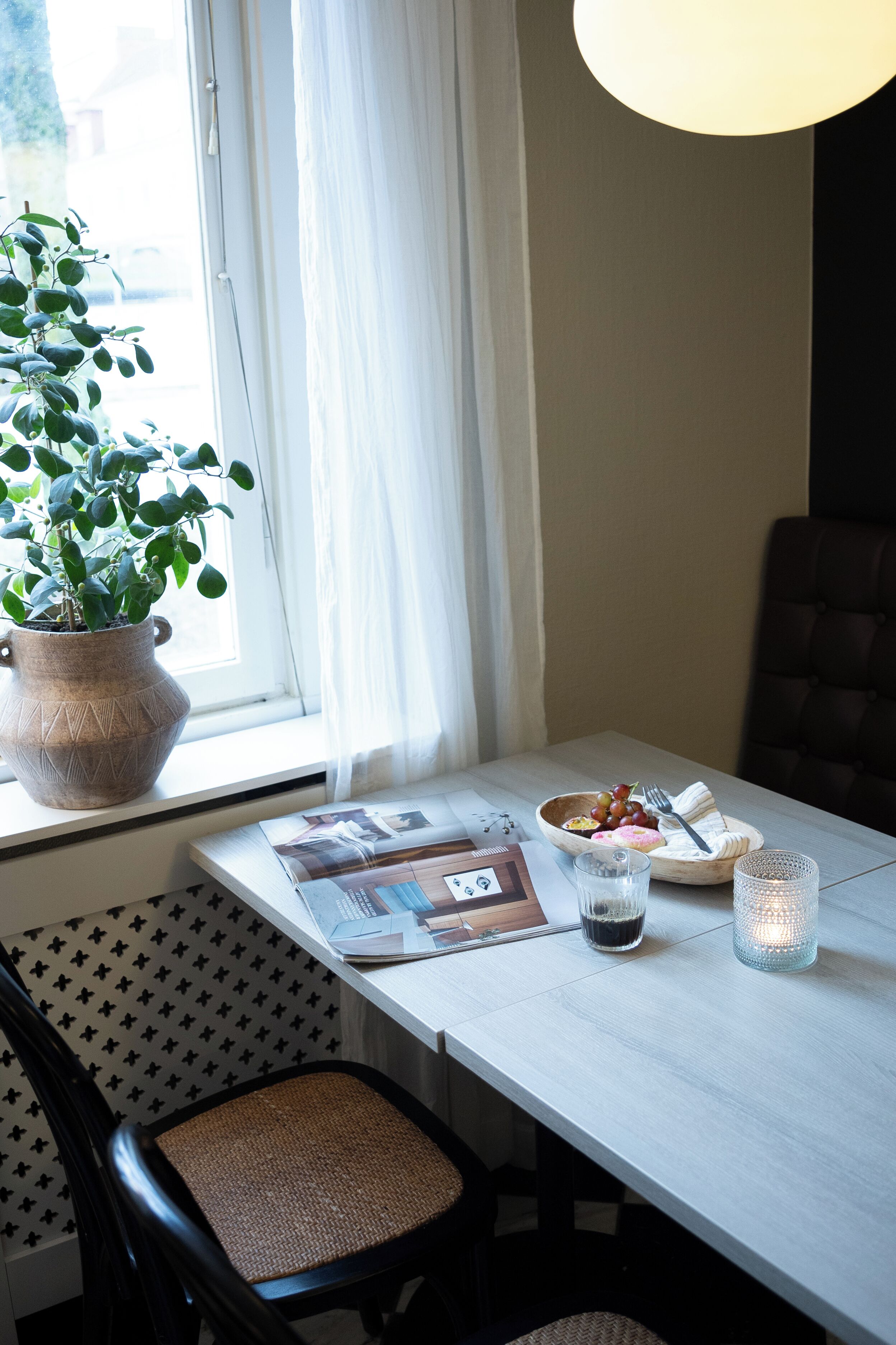 A dining area with a table set for two, a potted plant, and a window with curtains.
