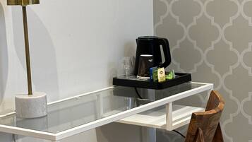 A modern room with a white desk, a wooden chair, a floor lamp, and a coffee maker.