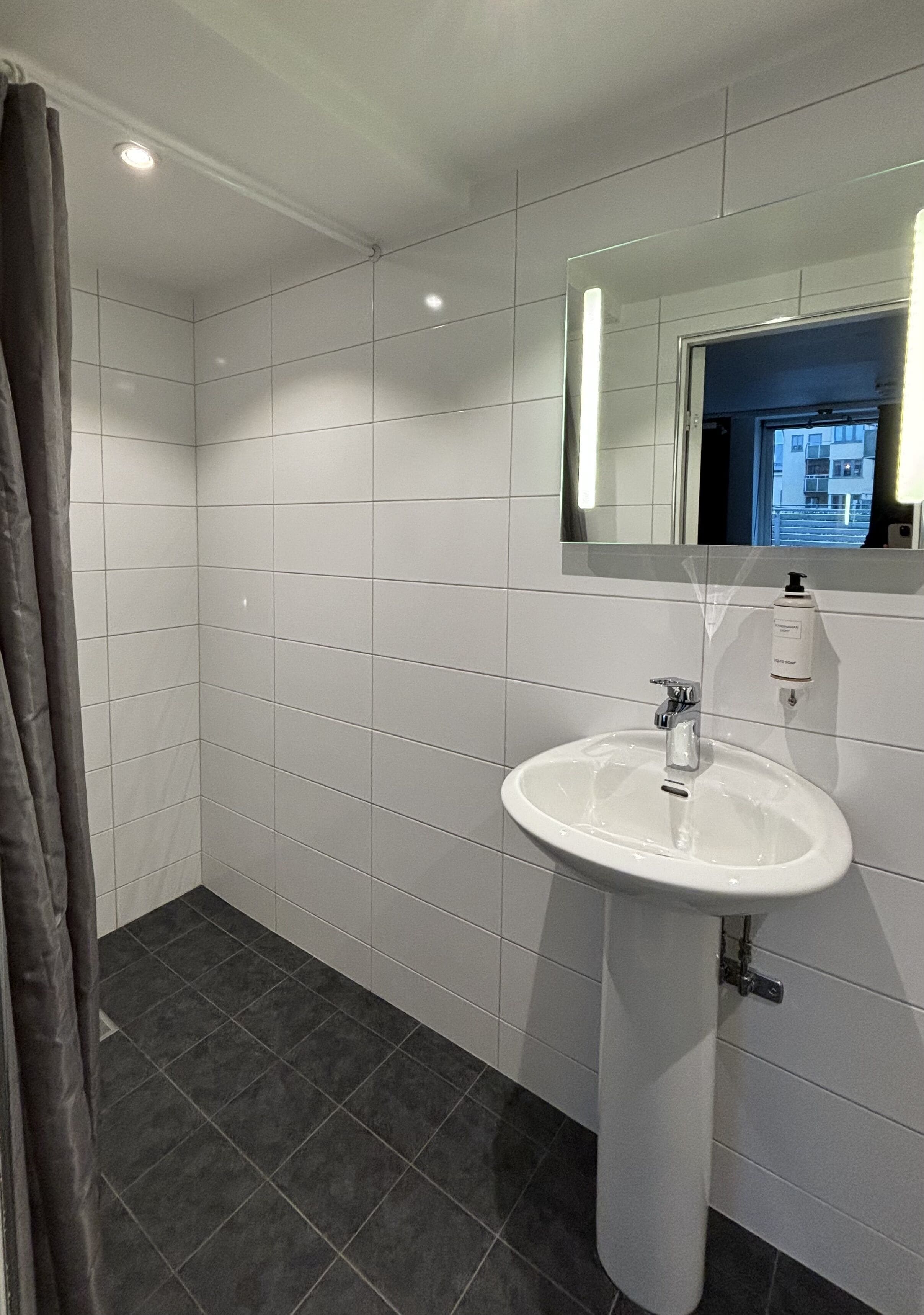 A modern bathroom with white tiles, a white sink, and a mirror.