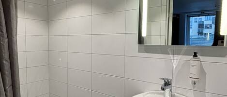 A modern bathroom with white tiles, a white sink, and a mirror.