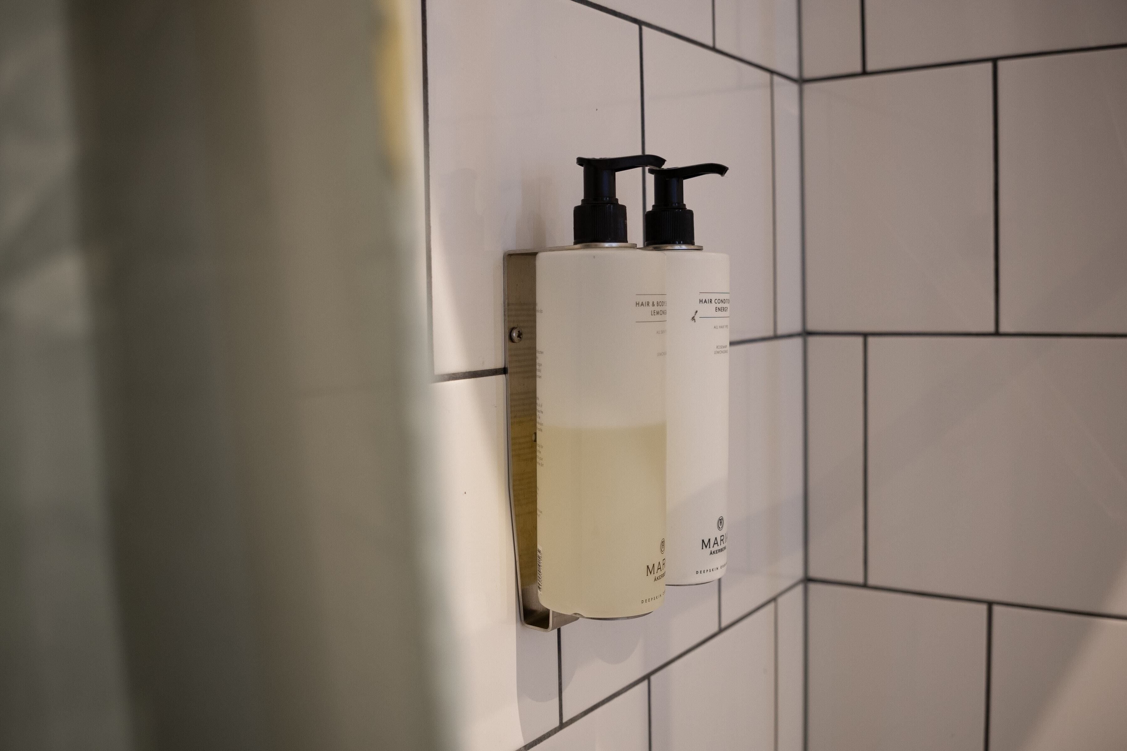Un baño con paredes de azulejos blancos y un dispensador fijado a la pared.