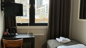Een hotelkamer met een bed, een bureau met een beeldscherm, een stoel, een radiator en een raam met gordijnen.