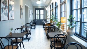 A restaurant with a long, narrow layout, featuring tables and chairs arranged along the walls, large windows on one side, and framed botanical prints on the walls. - Hotell Esplanad (Växjö)