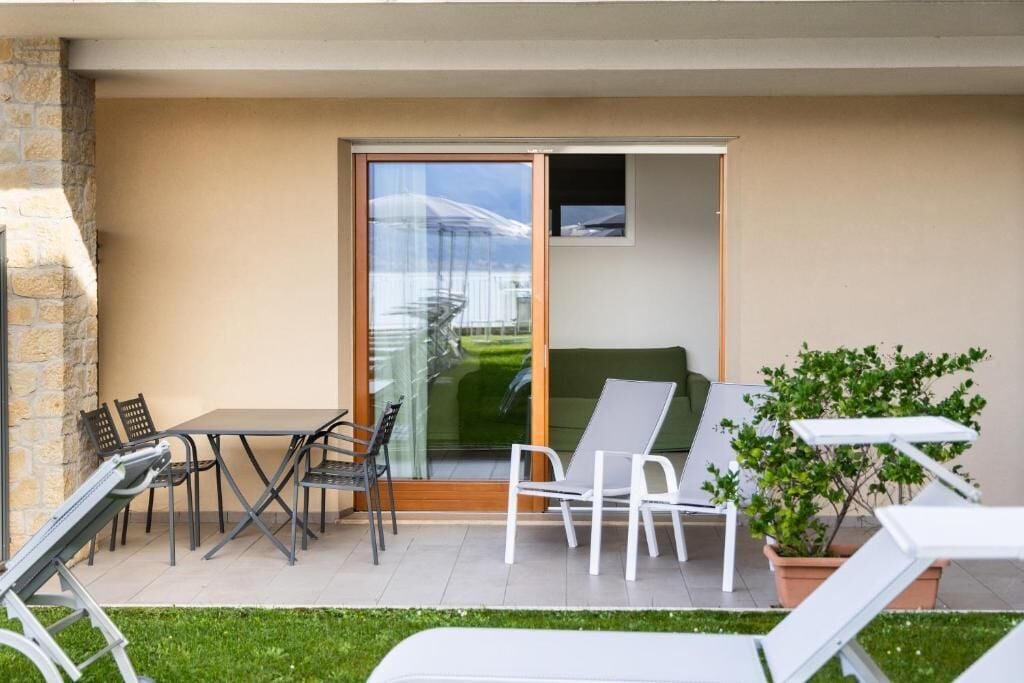 A modern outdoor patio with a table and chairs, a sliding glass door leading to a balcony, and a potted plant.
