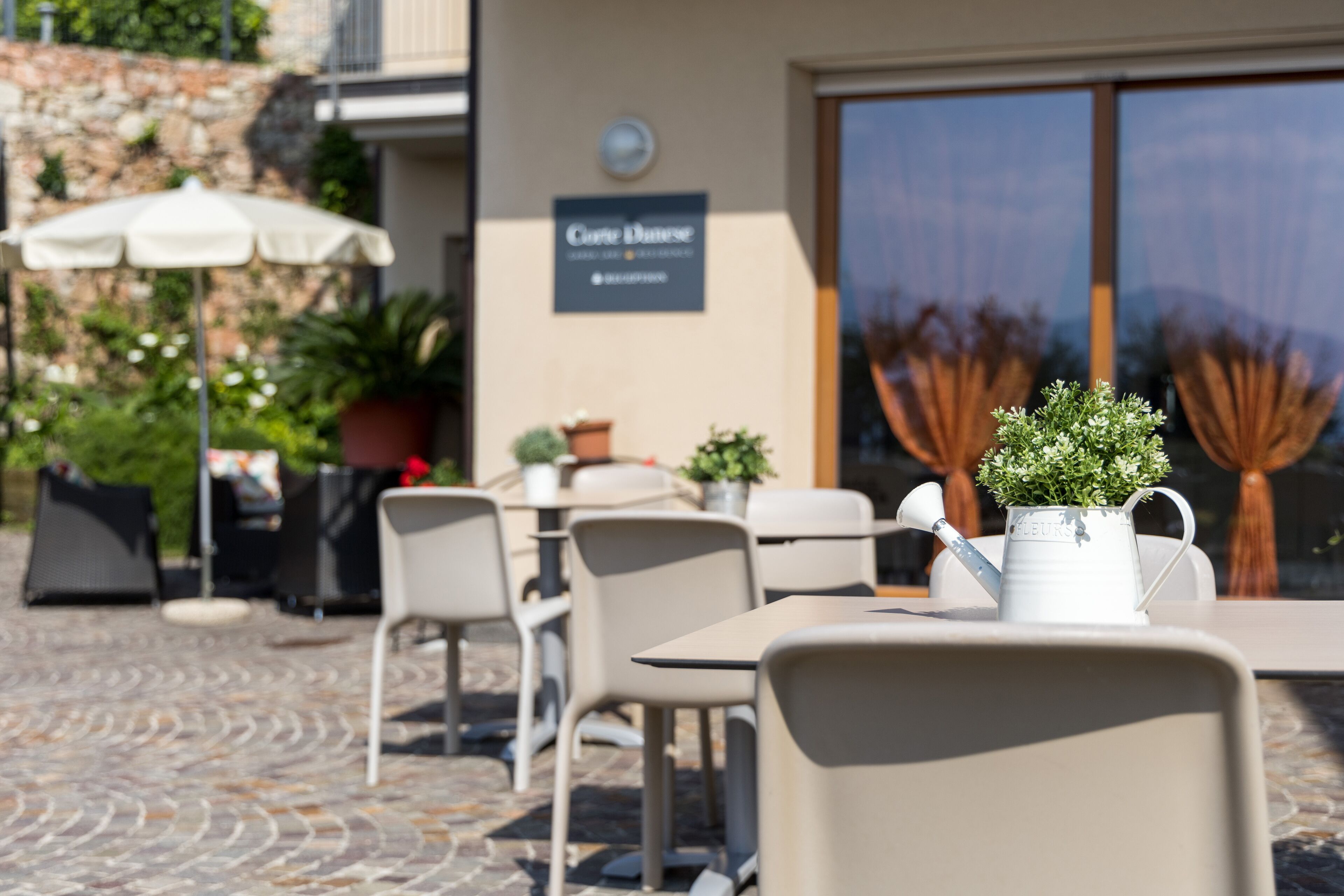 An outdoor cafe area with tables and chairs, potted plants, and a sign for 'Café Dune'.