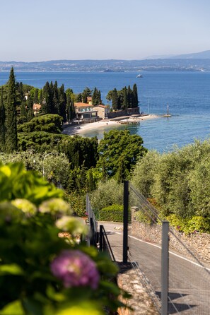 A coastal view with a beach, a boat, and a building with a garden. - Residence La Corte Danese (Torri del Benaco)