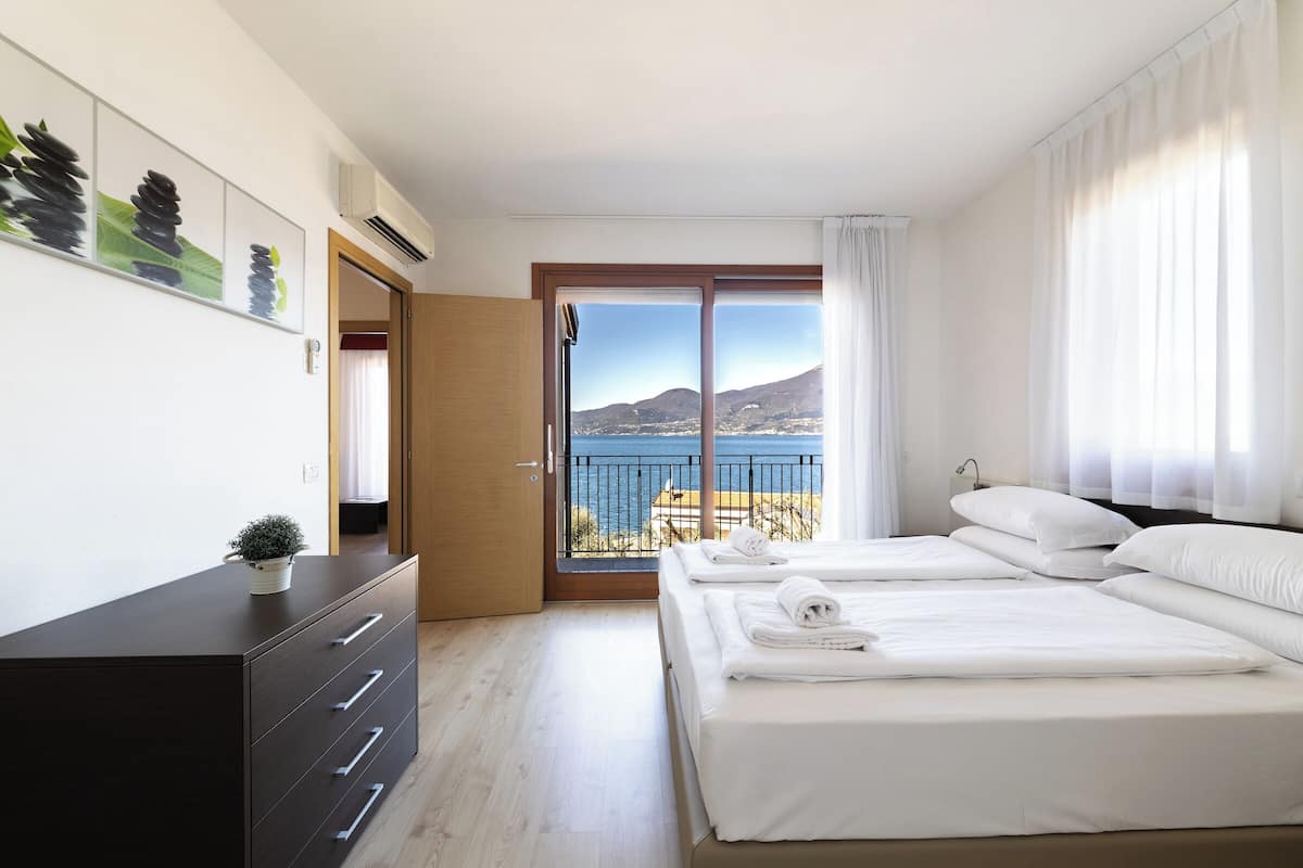 A hotel room with two beds, a dresser, and a view of the sea.