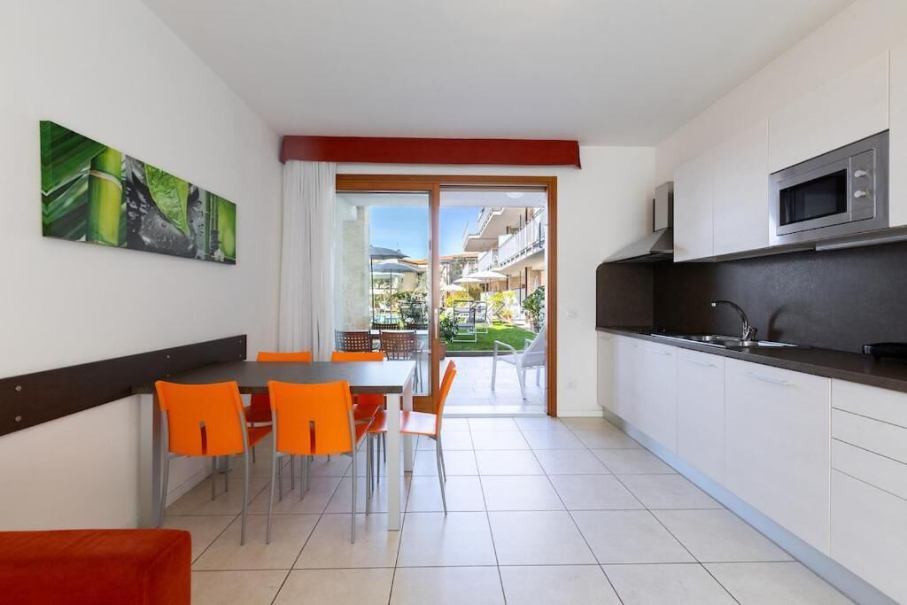 A modern kitchen with white cabinets, a stainless steel microwave, and a dining area with orange chairs.