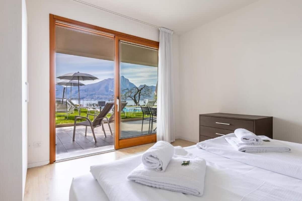 A hotel room with a bed, a wooden nightstand, and a view of a pool and mountains.
