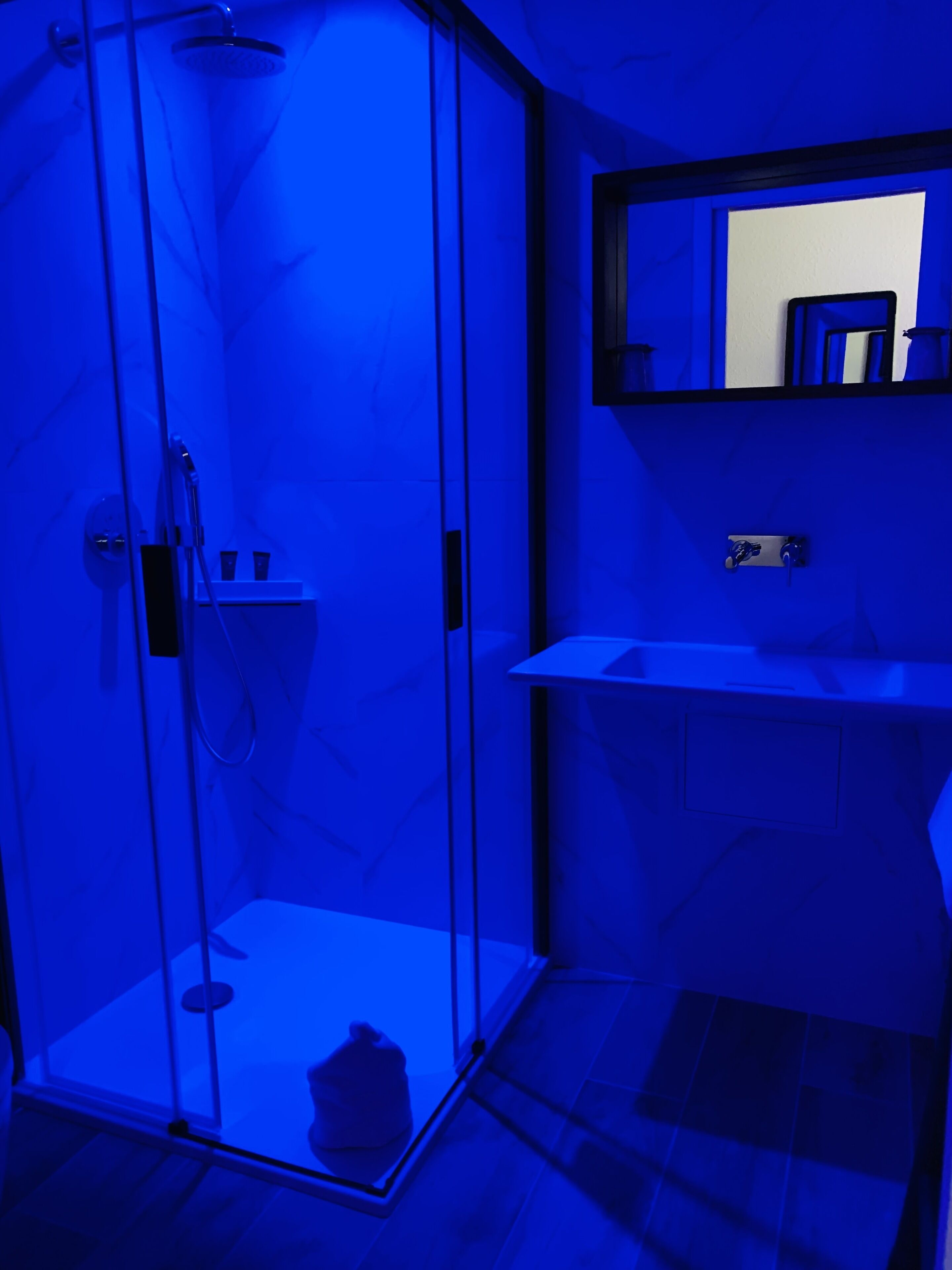 Bany amb dutxa de vidre, un lavabo blanc i un mirall sobre el lavabo.
