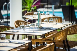 A dining area with wicker chairs and tables, each set with cutlery and glasses.