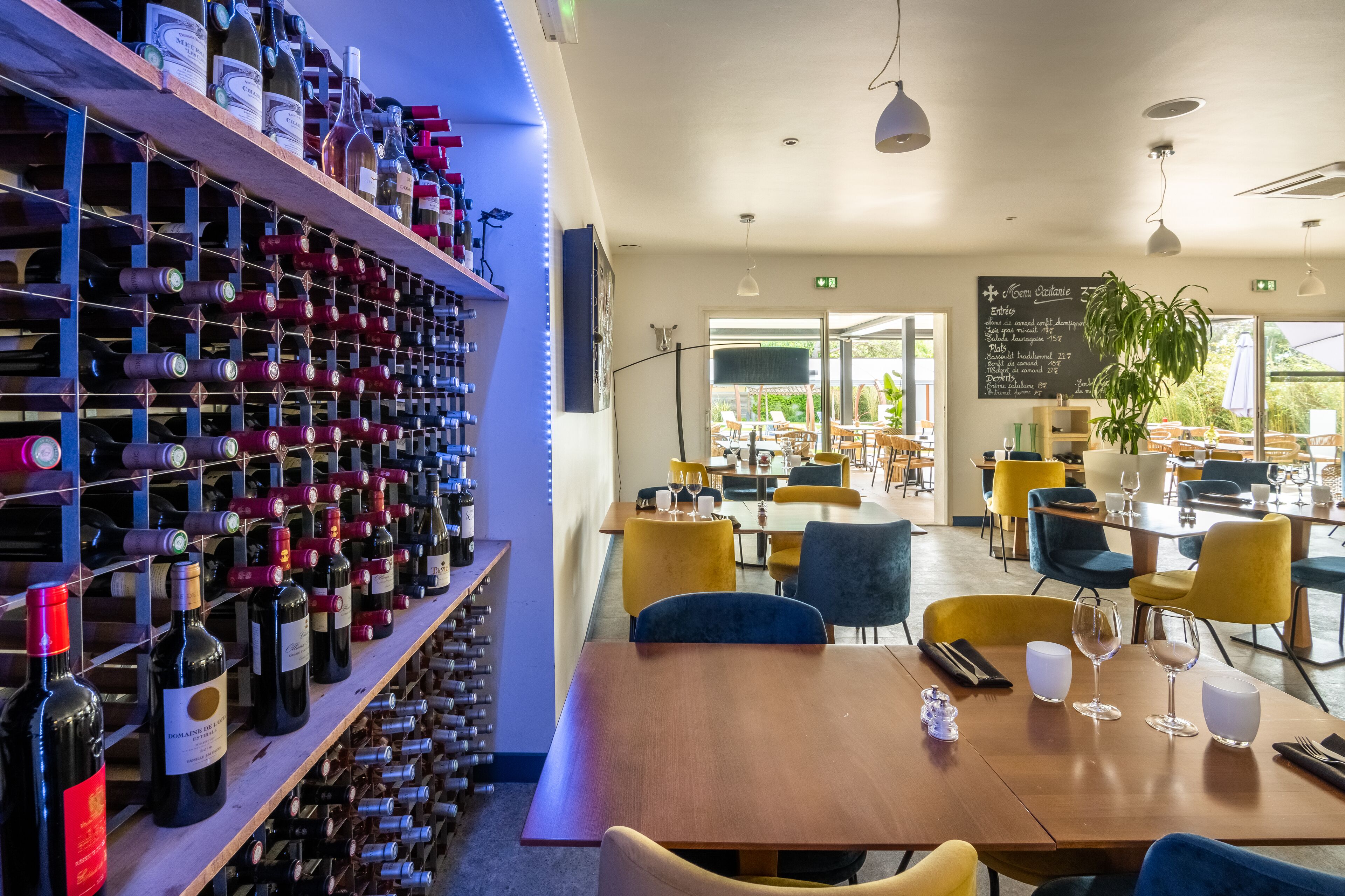 A restaurant with a wine rack, tables, chairs, and a menu board.