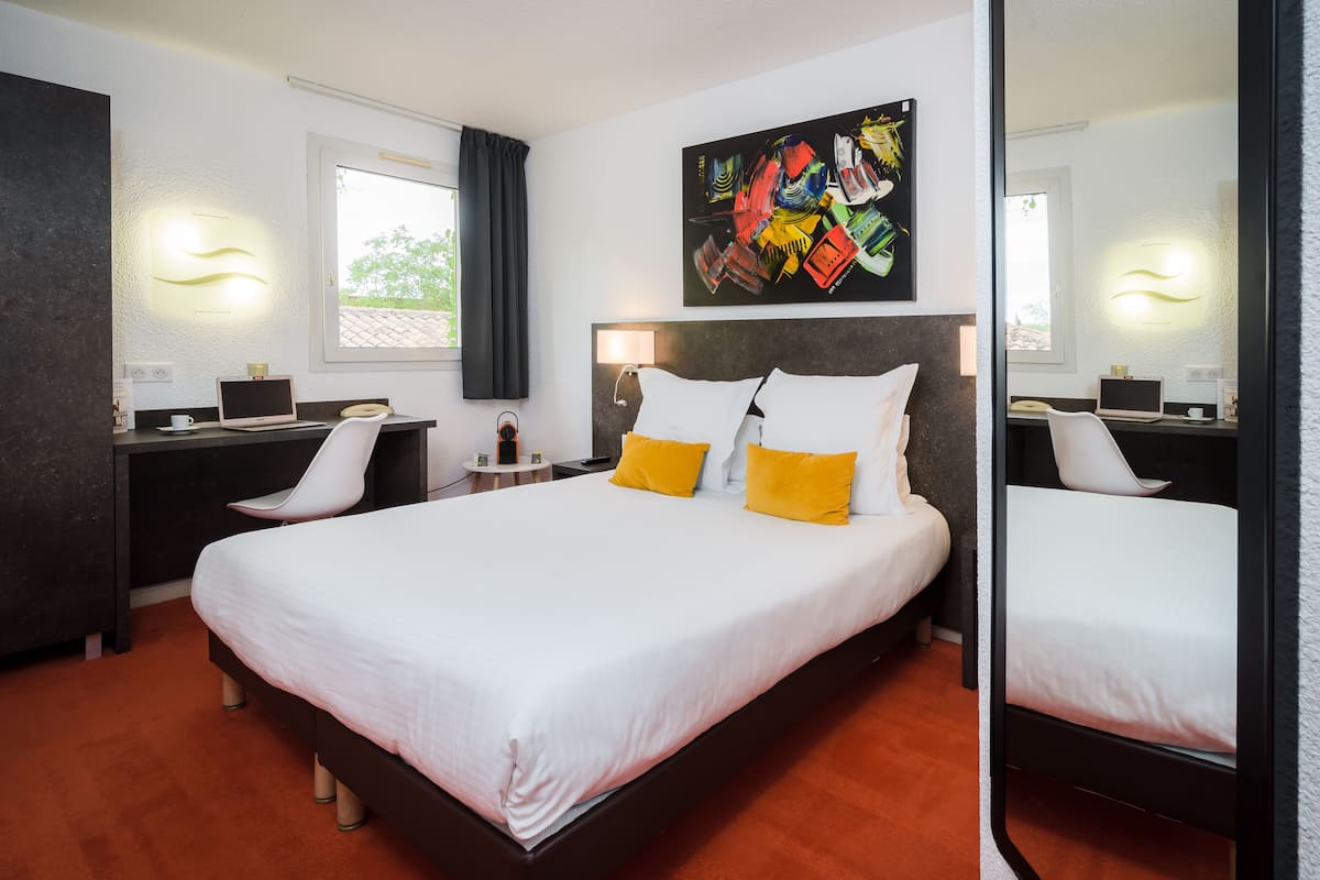 Habitación de hotel moderna con una cama grande, un escritorio y una silla. Hay un cuadro en la pared y una ventana con cortinas.