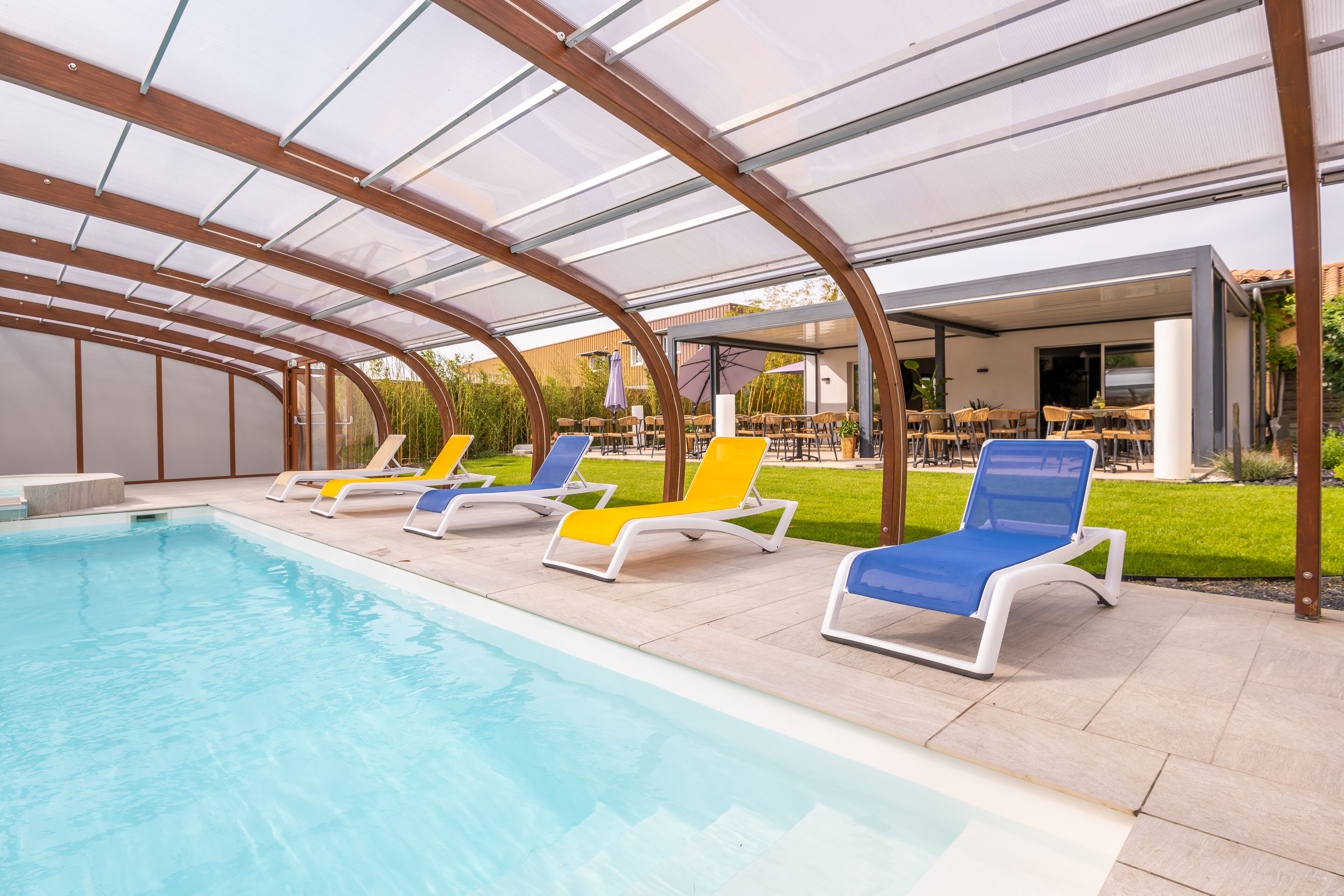 Un área de piscina con sillones de descanso y un porche cubierto.
