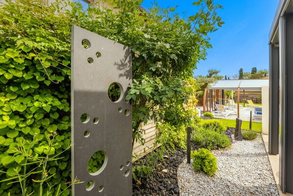 Edificio moderno con estructura metálica y recortes circulares, rodeado de abundante vegetación y un jardín cuidado con senderos de grava.