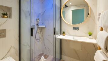 A modern bathroom with a glass-enclosed shower, a round mirror, and a white sink.