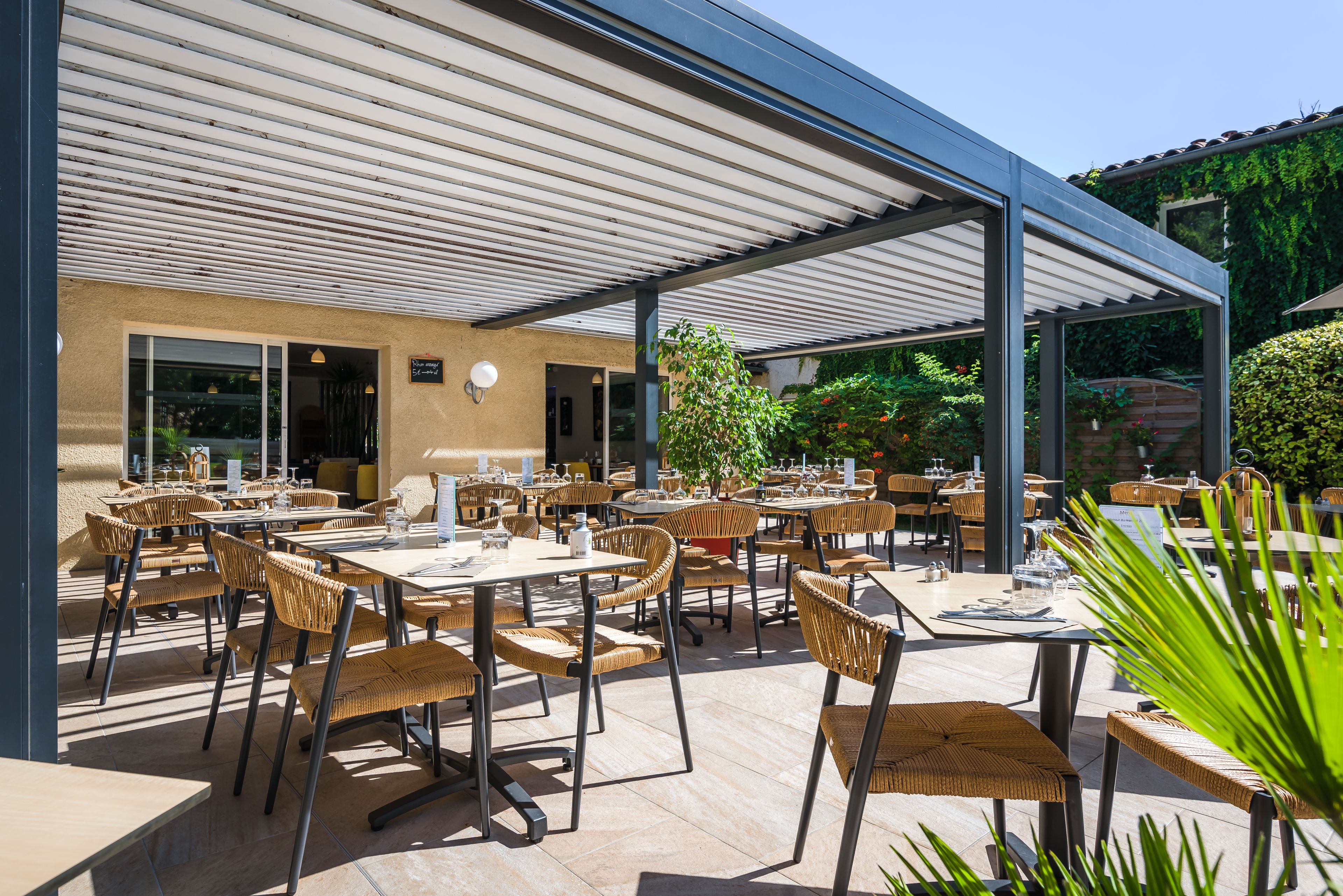 An outdoor patio with wicker tables and chairs, a covered seating area, and a view of the surrounding garden.