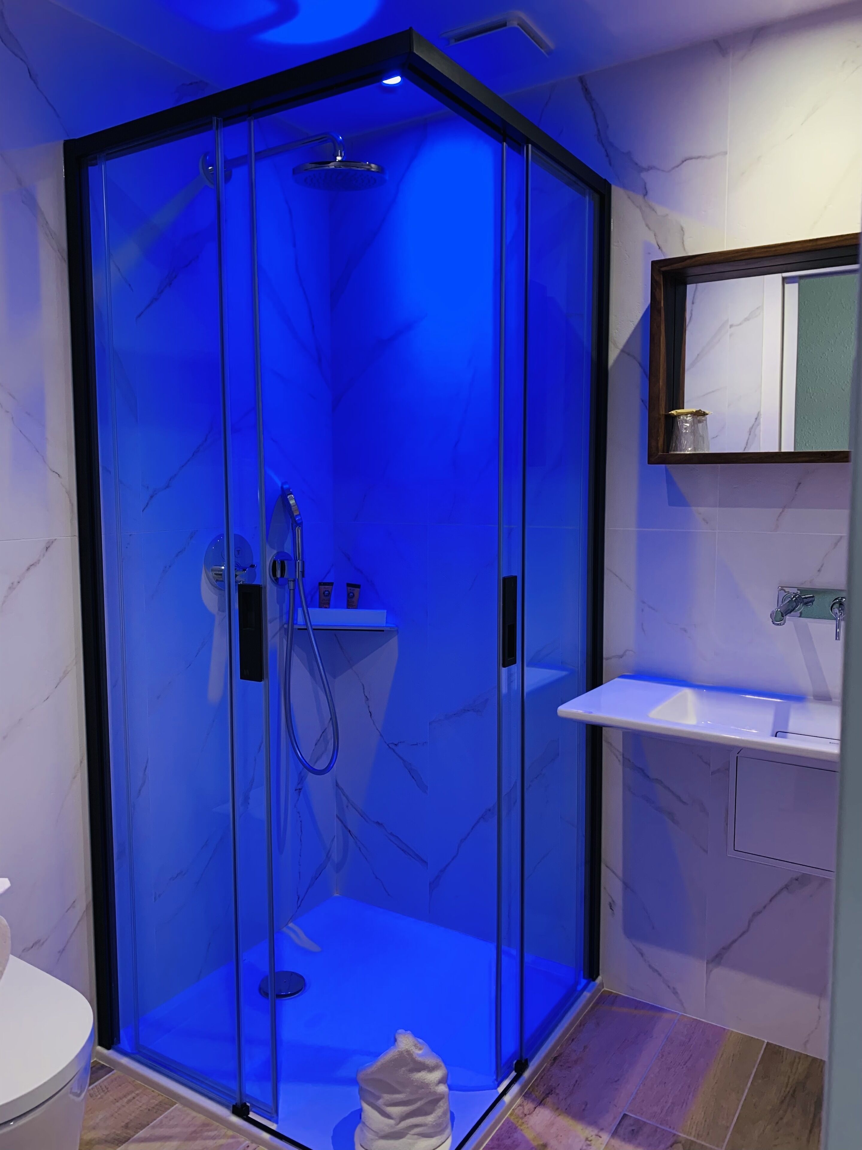Un baño moderno con ducha de vidrio, lavamanos blanco y piso de mármol.