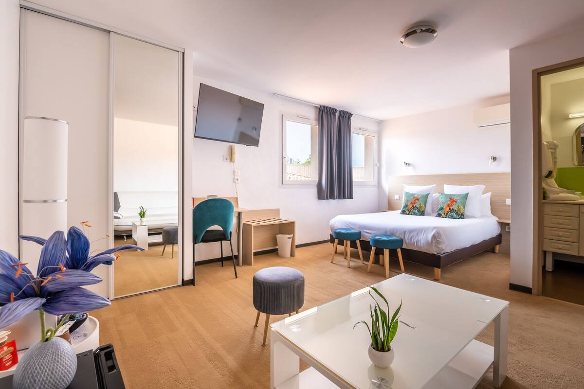 Habitación de hotel moderna con cama, escritorio, silla y una mesita con una planta.