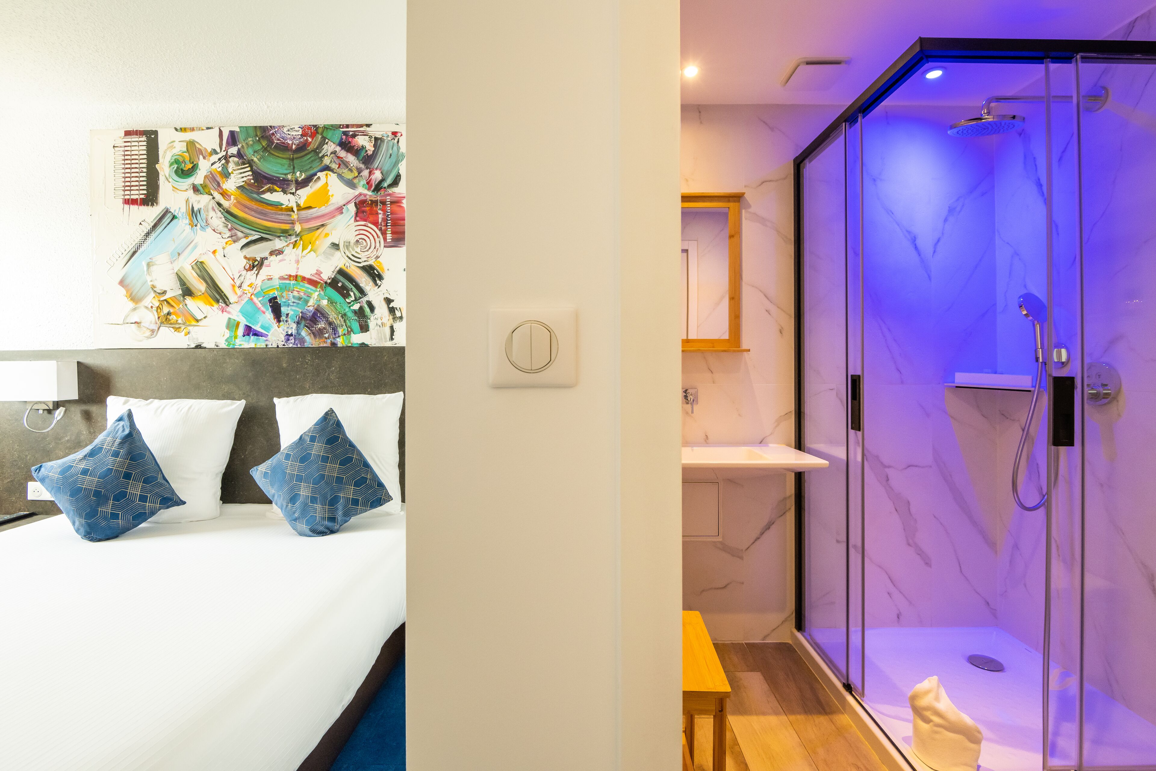 Camera d'albergo con un letto, un'opera d'arte a parete, un bagno con doccia a vetro e pareti in marmo.