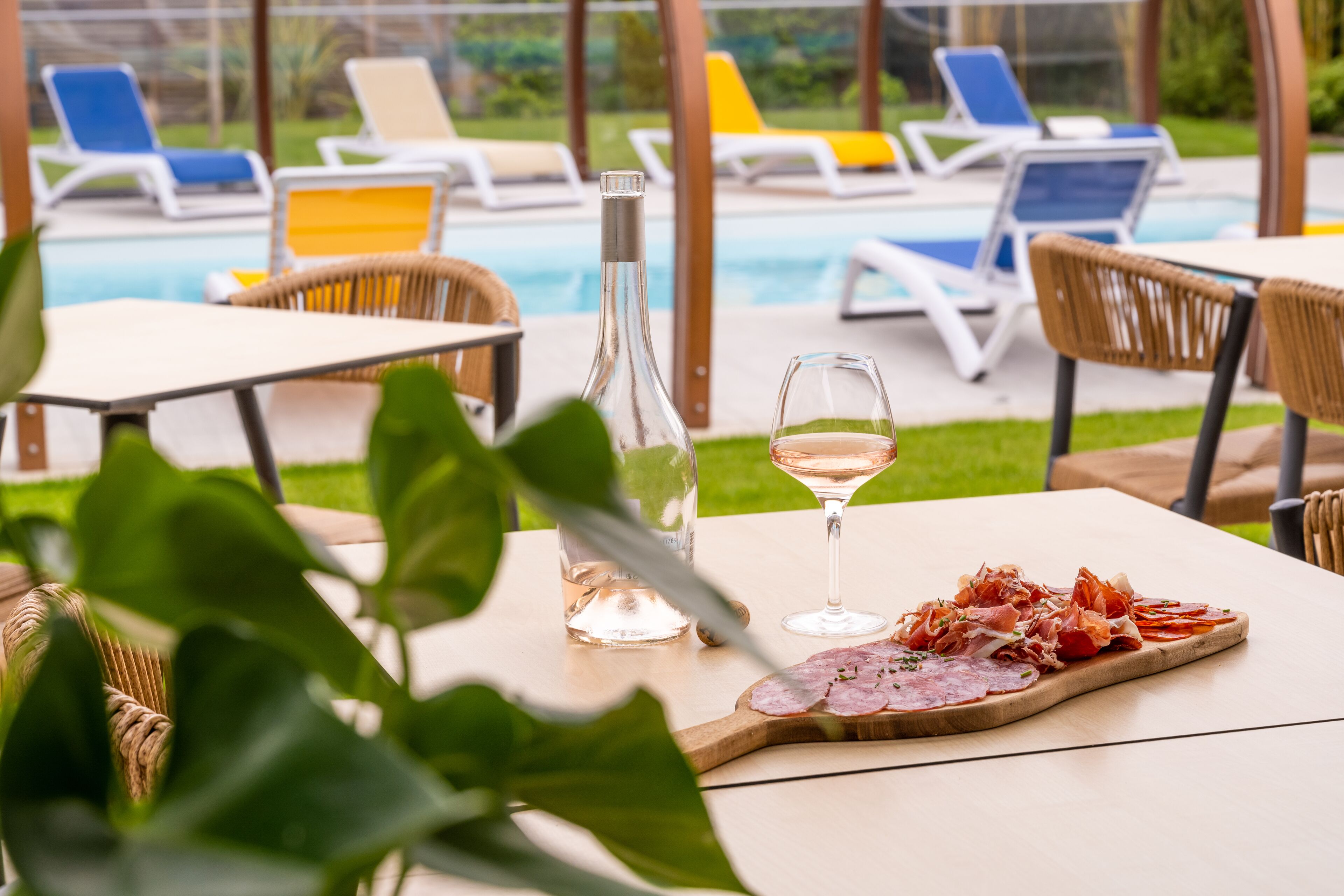 Une table avec une bouteille, un verre et une assiette de nourriture, entour ée de fauteuils et avec une piscine en arrière-plan.