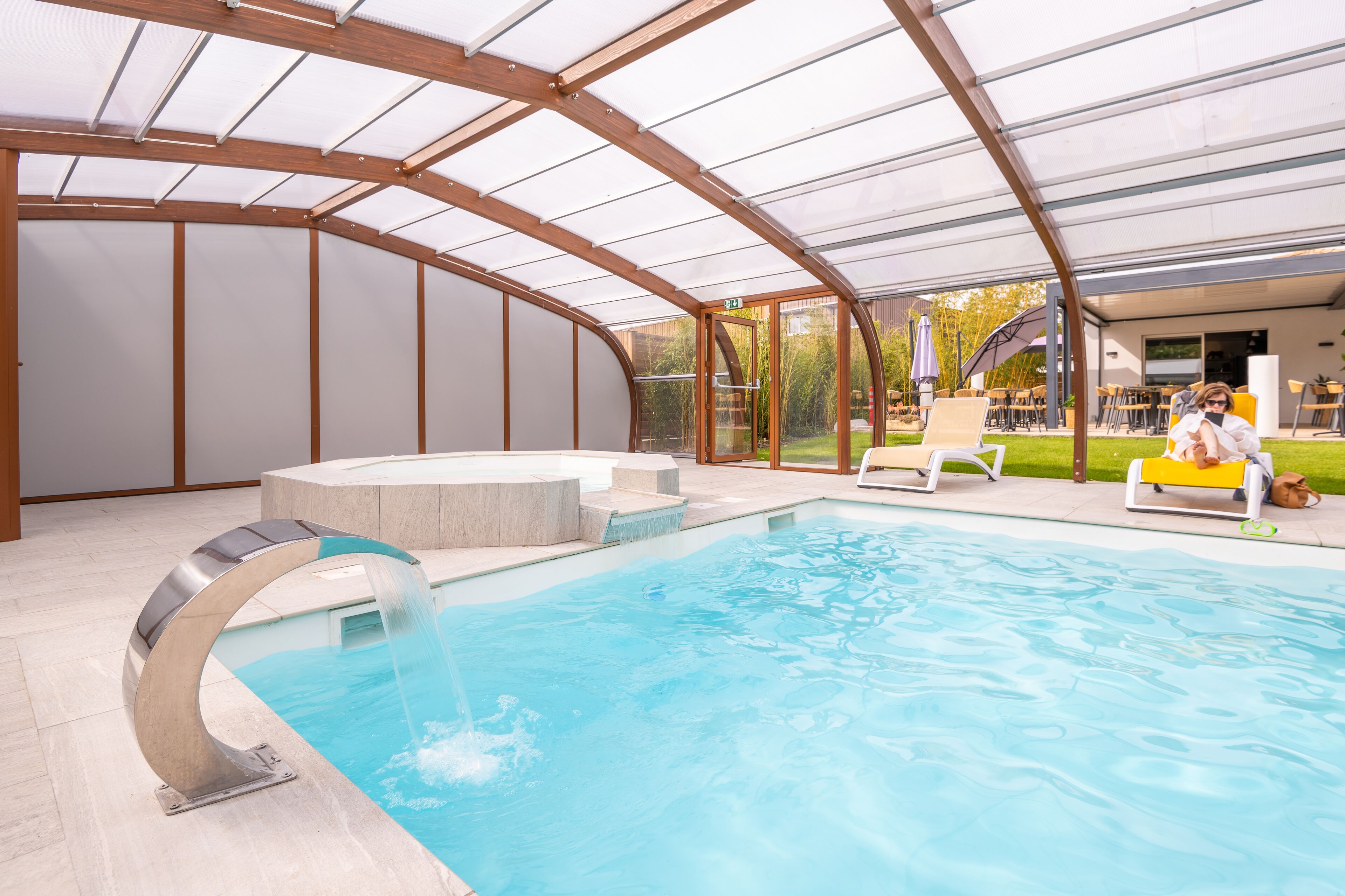 Una piscina interior con techo de vidrio, un jacuzzi y sillones de descanso.