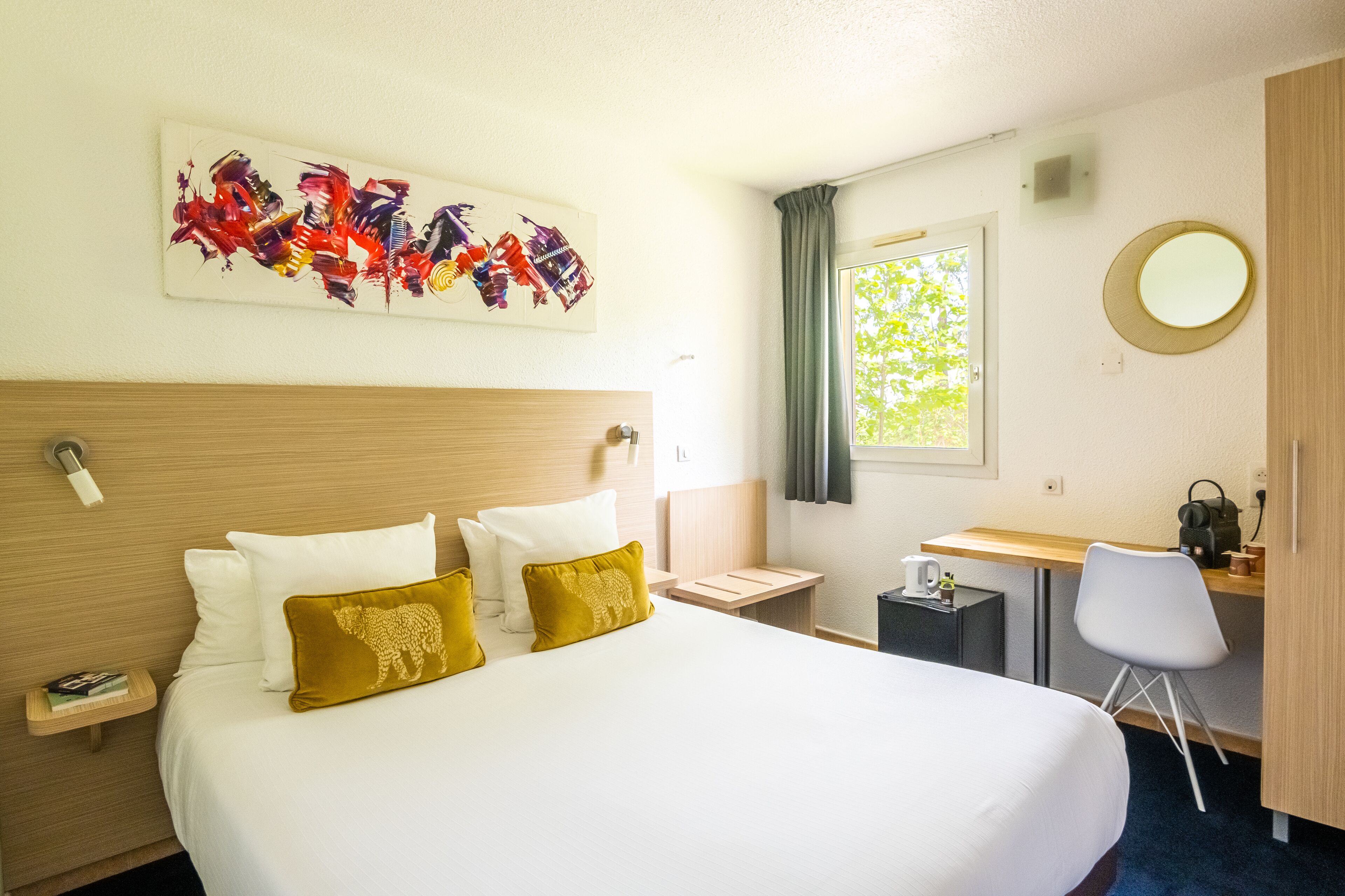 A hotel room with a large bed, a desk, a chair, a window, and a painting on the wall.