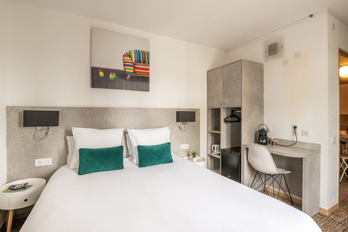 Una habitación de hotel moderna con una cama grande, dos mesitas de noche, un escritorio con silla y un armario.