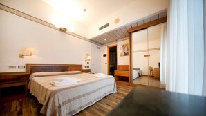 A hotel room with two beds, wooden flooring, a large mirror, and a wooden bench. - Hotel Marina Bay (Rimini)