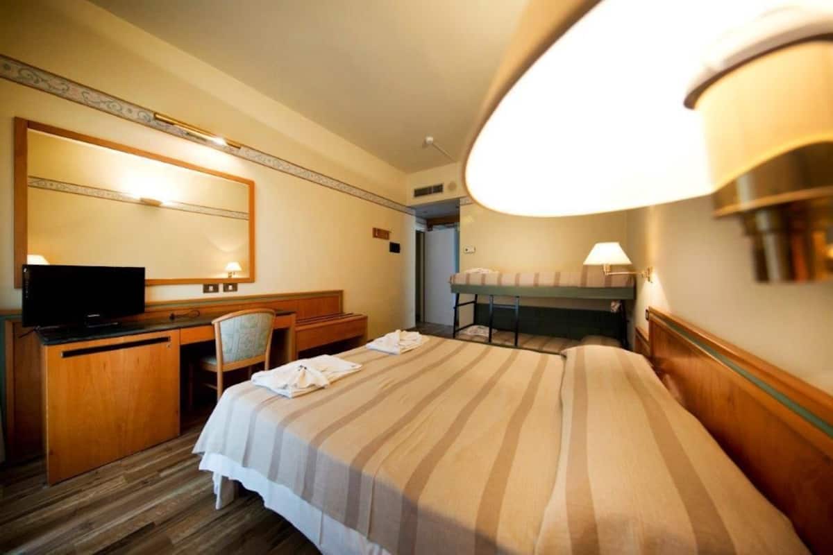 A hotel room with a bed, a desk, a chair, a television, and a lamp.
