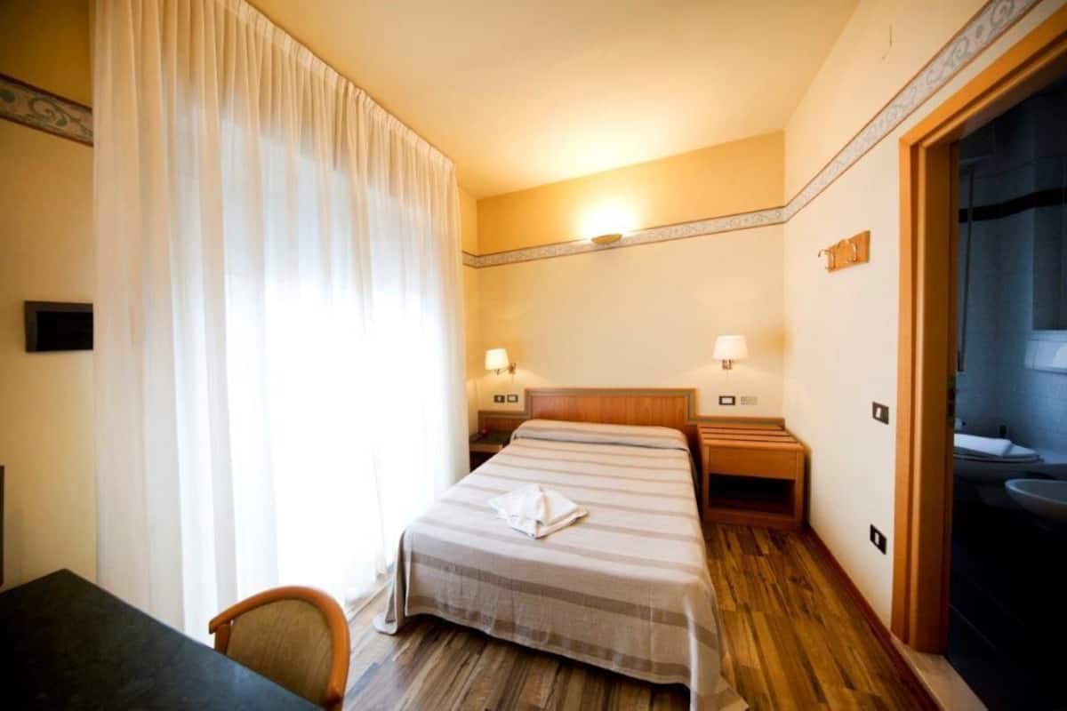 A hotel room with a bed, bedside tables, a chair, a desk, and a bathroom with a sink and mirror.