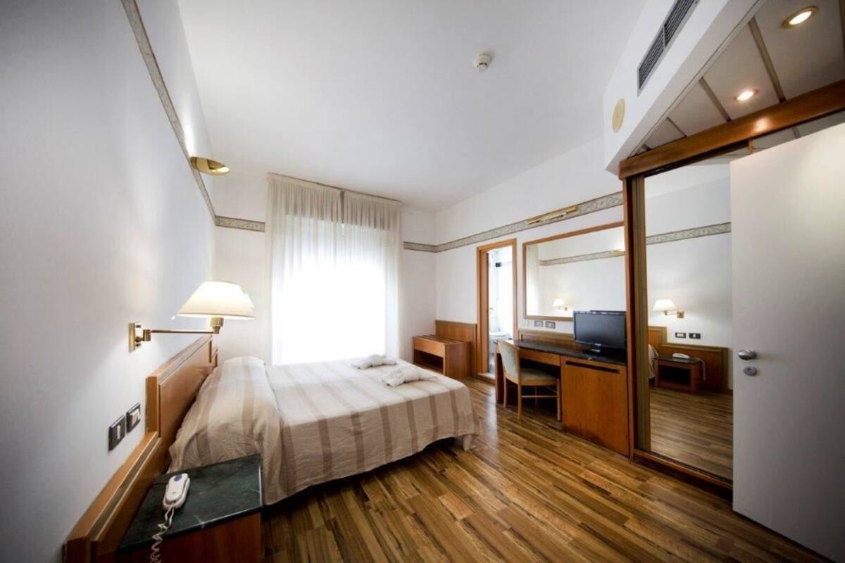 A hotel room with a bed, desk, TV, and a mirror.