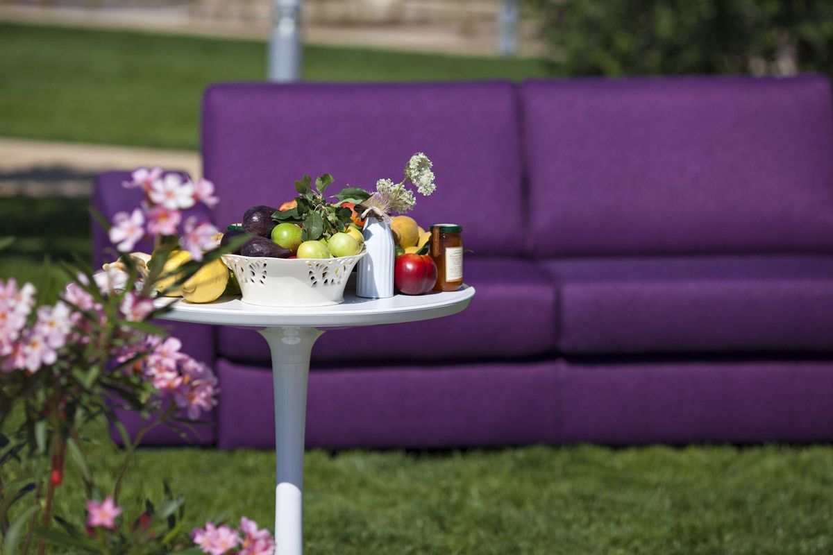 A table with a fruit basket and a bottle in front of a purple couch.