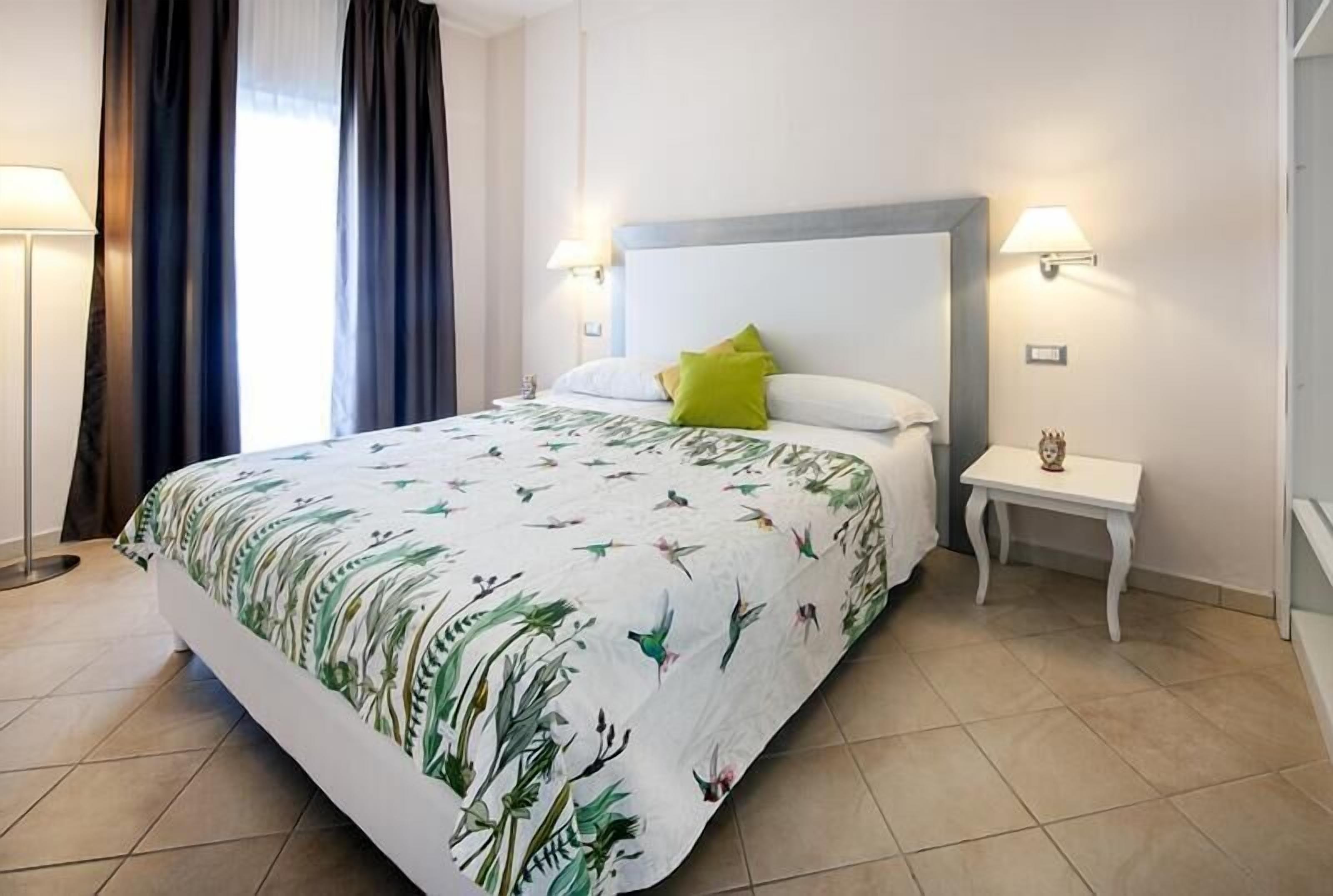 A neatly made bed with a floral bedspread, two bedside lamps, and a small bedside table with a decorative item.