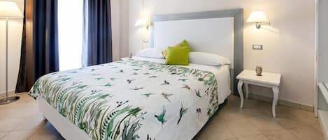 A neatly made bed with a floral bedspread, two bedside lamps, and a small bedside table with a decorative item.