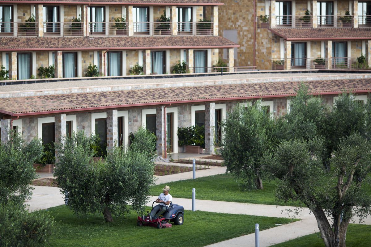 A multi-story building with balconies and a lawn area where a person is riding a lawn mower.