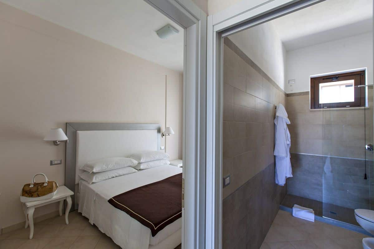 A hotel room with a bed, bedside table, lamp, and a view into the bathroom.