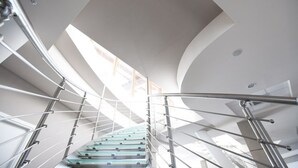 Una escalera moderna con barandillas de metal y balaustrada de vidrio, que conduce a un piso superior.