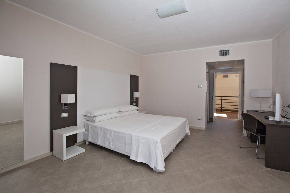 A modern hotel room with a large bed, bedside tables, a desk, and a chair.