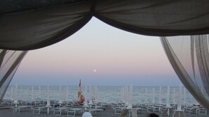 Una playa con filas de tumbonas y sombrillas, un bote y vista al mar y la luna.