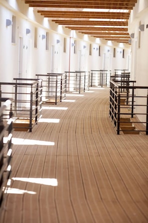 A hotel corridor with wooden beams, metal railings, and a patterned floor.