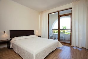 A bedroom with a bed, a nightstand, a window with curtains, and a view of an outdoor area. - Sunrise Club Apart Hotel (Ravda)
