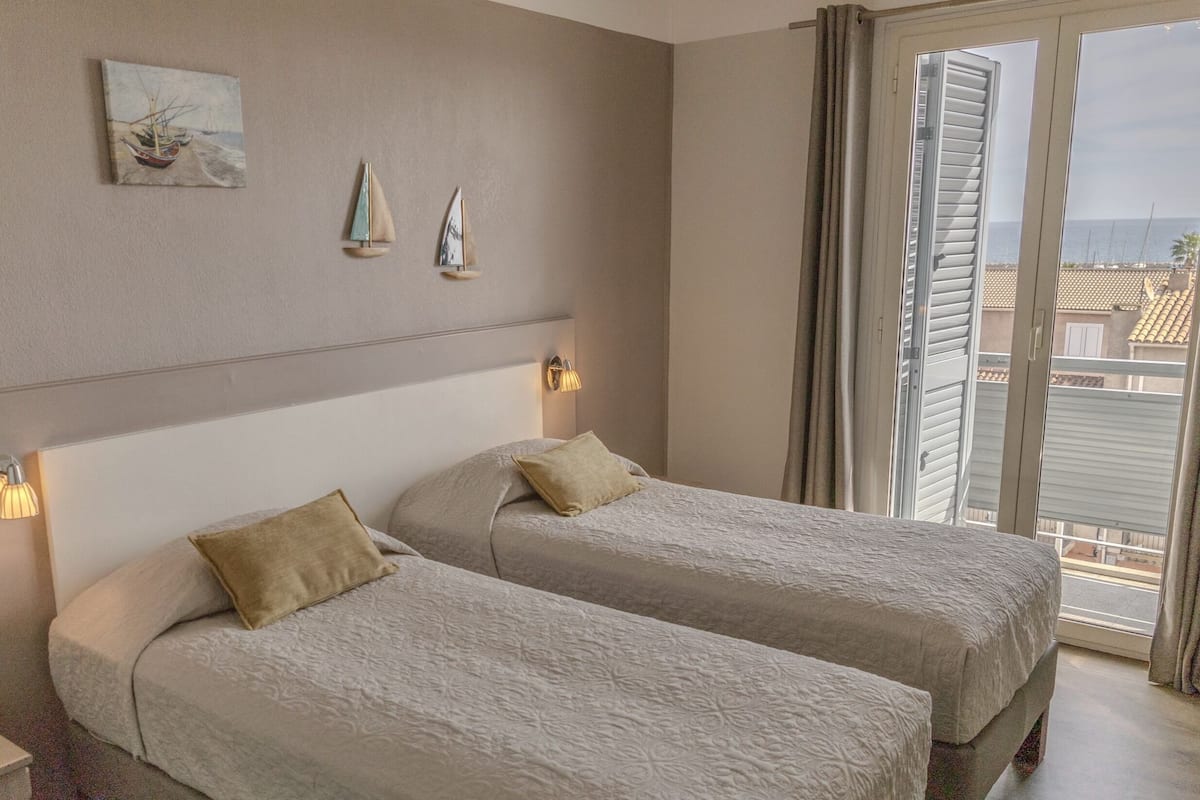 A hotel room with two beds, a painting, and a view of the sea.
