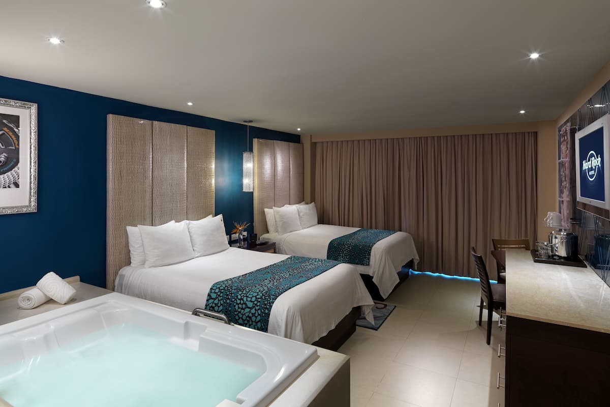 A hotel room with two beds, a large bathtub, a desk, and a minibar.