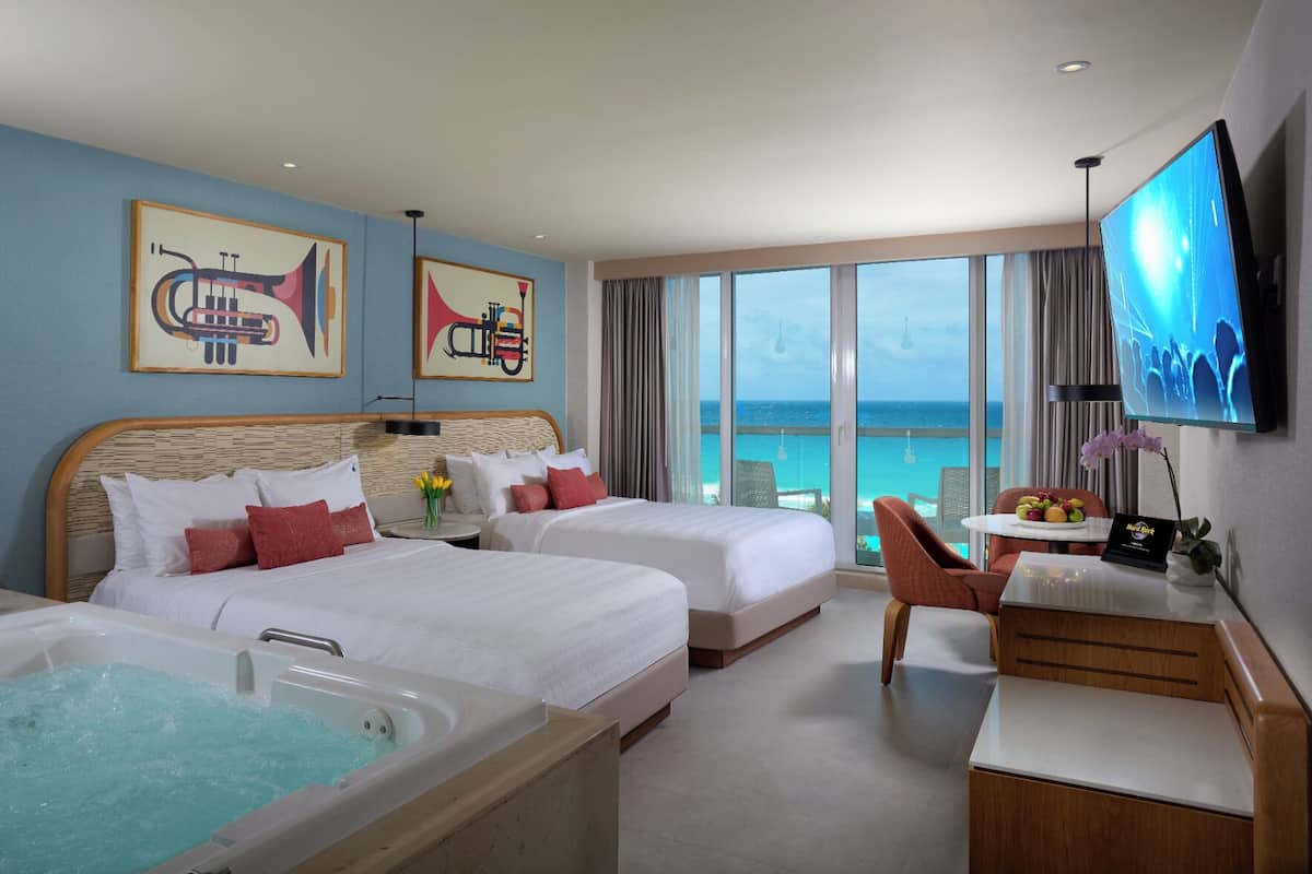 A hotel room with two beds, a bathtub, a TV, and a view of the ocean.