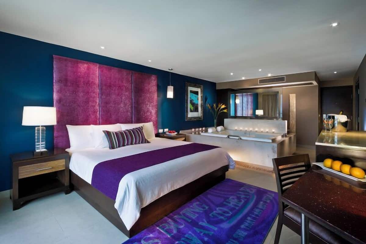 A modern hotel room with a large bed, a sitting area with a table, and a separate bathroom.
