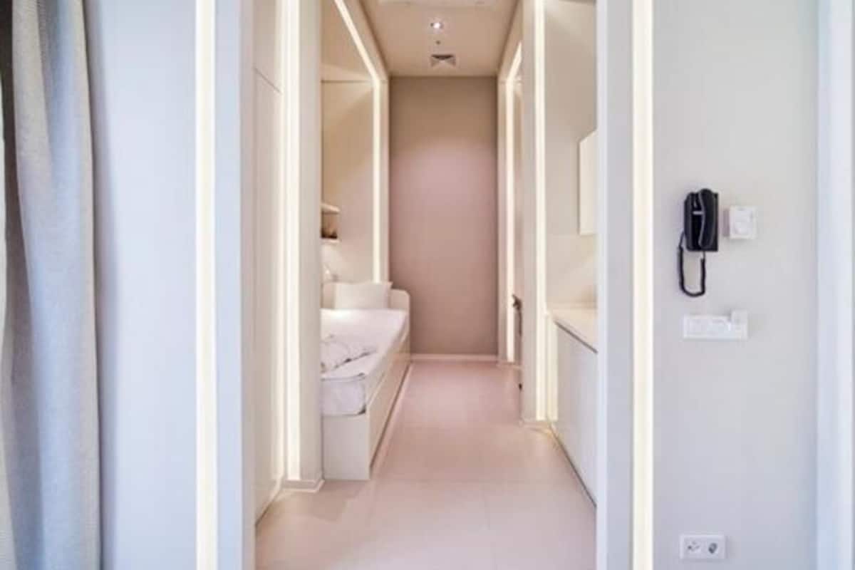Un pasillo estrecho con una cama al fondo, un teléfono en la pared y un interruptor de luz.